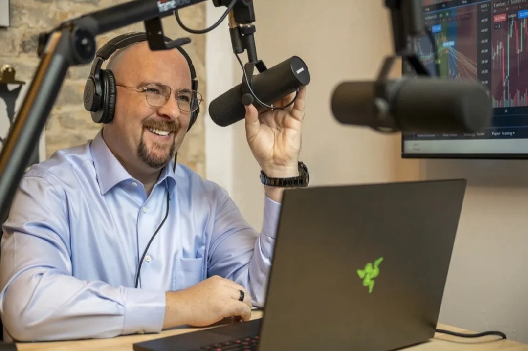 Sean Donahoe at his desk, on the mic, with the charts up behind him