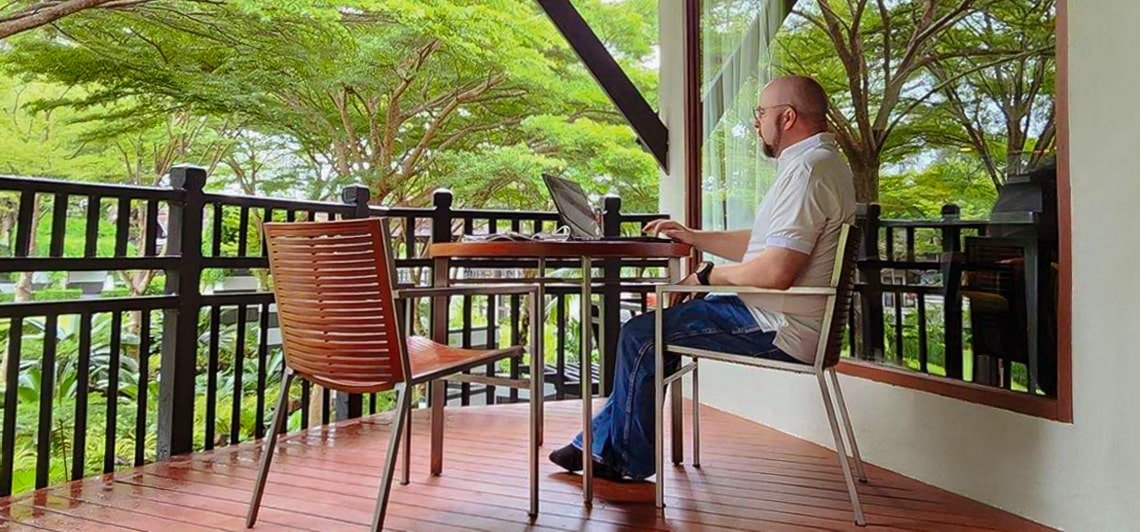 Sean Donahoe on a balcony in Thailand with one laptop on a small table